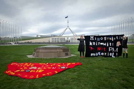 Two craftivists from Knit Your Revolt hold up knitted banners in front of Parliament House in Canberra, February 2015