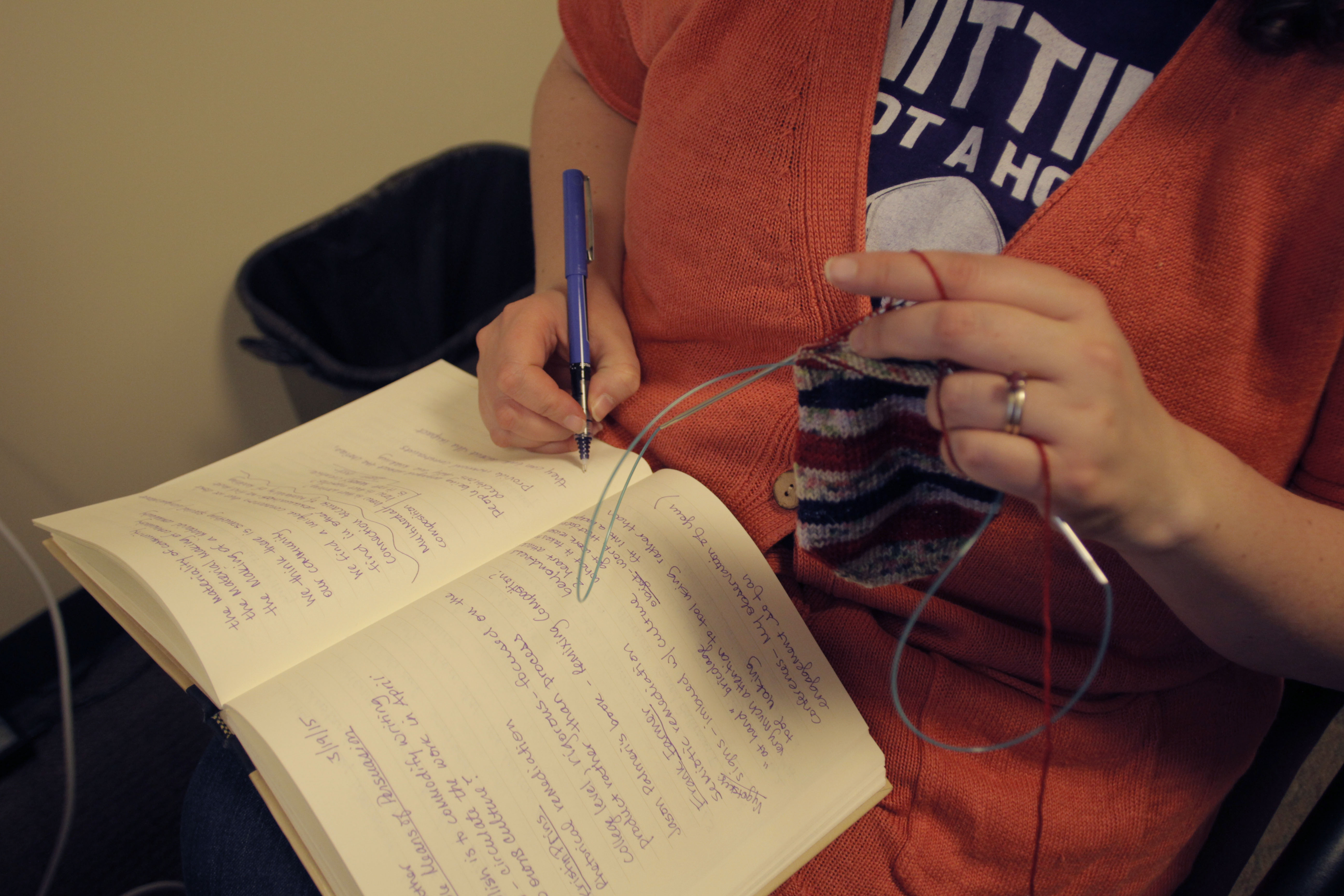 Hannah writing in her notebook and knitting